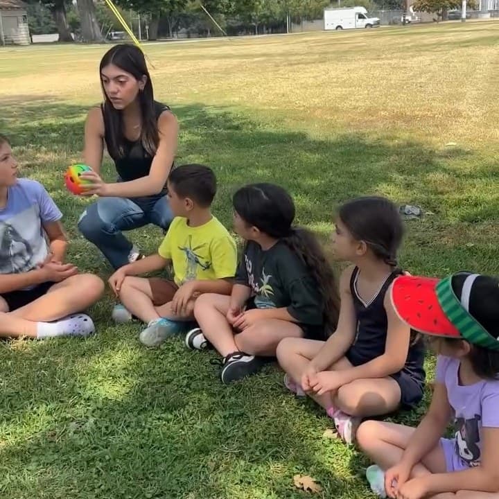 Campers sitting on the grass with a counselor at the park